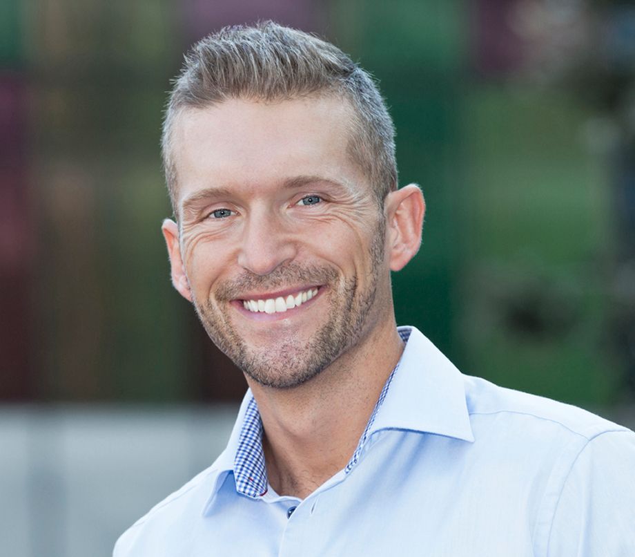 Smiling man in a light blue shirt outdoors.