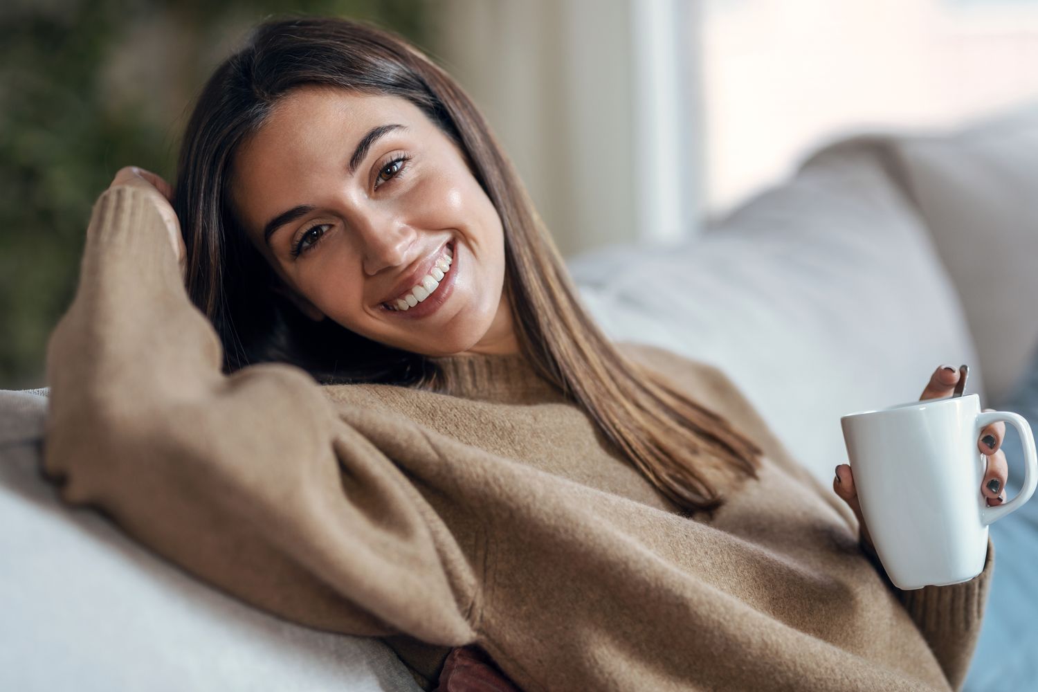 Smiling woman enjoying a warm beverage indoors.
